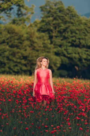 Beautiful woman enjoying nice day in poppy field, wearing red dressの写真素材