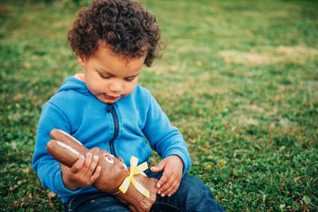 Adorable two year old african toddler boy eating chocolate bunny on backyardの写真素材