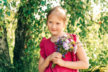 Summer portrait of cute little girl holding small bouquet of wild flowersの写真素材