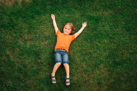 Happy child having fun outdoors. Kid playing in summer park. Little boy lying on green fresh grass, top viewの写真素材