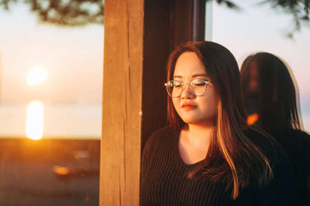 Outdoor portrait of asian plus size model at sunset, wearing eyeglasses