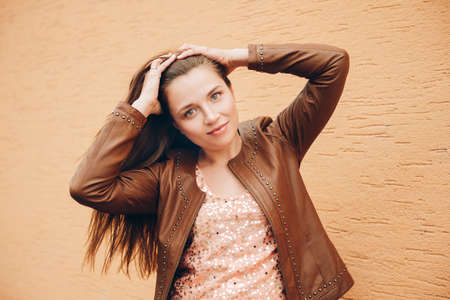 Outdoor portrait of young woman with long dark hair, wearing brown leather jacket