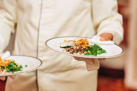 Waiter carrying two plates with fish and rice dish on some festive event, party, wedding reception or catered eventの写真素材