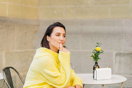 Outdoor fashion portrait of beautiful woman with dark hair, wearing yellow pullover, posing in...