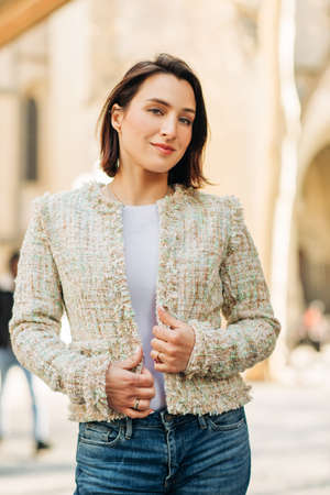 Outdoor fashion portrait of beautiful woman with dark hair, wearing fashionable tweed jacket, posing...