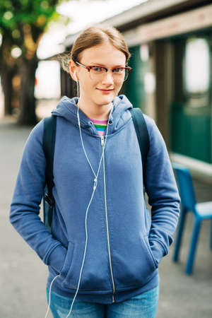 Outdoor portrait of young preteen girl wearing backpack and eyeglasses, listeming music with earphonesの写真素材