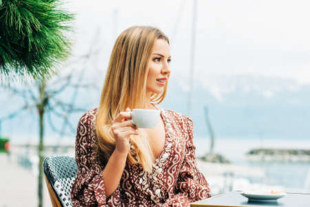 Outdoor portrait of beautiful woman resting in cafe with cup of coffee