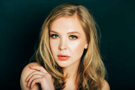 Close up portrait of beautiful young woman with blond hair and professional make up, posing on black backgroundの写真素材
