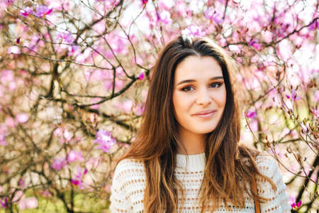 Outdoor portrait of beautiful young woman wearing white pullover, posing in pink flowers