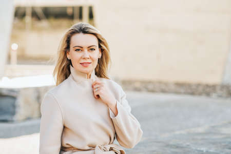 Outdoor portrait of beautiful blond woman wearing beige belted coatの写真素材