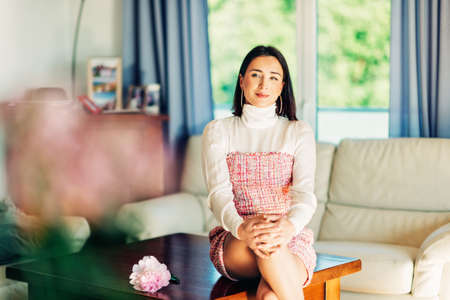 Interior portrait of beautiful woman with dark hair wearing fashionable clothes, sitting on the...