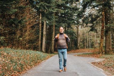Handsome middle age man hiking in forest, wearing pullover, backpack and glassesの写真素材