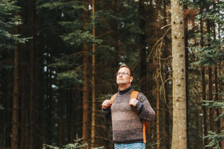 Handsome middle age man hiking in forest, wearing pullover, backpack and glassesの写真素材