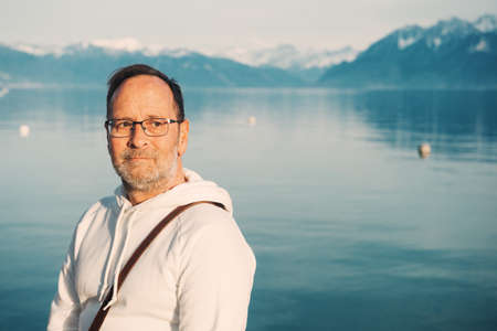 Portrait of handsome man admiring beautiful lake with mountains, wearing white sweatshirtの写真素材