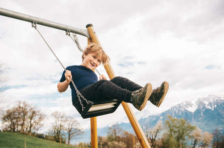 Kid boy having fun on swing in swiss alps, playground with beautiful viewの写真素材
