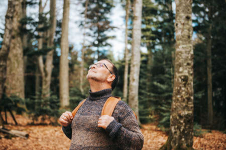 Handsome middle age man hiking in forest, wearing pullover, backpack and glassesの写真素材