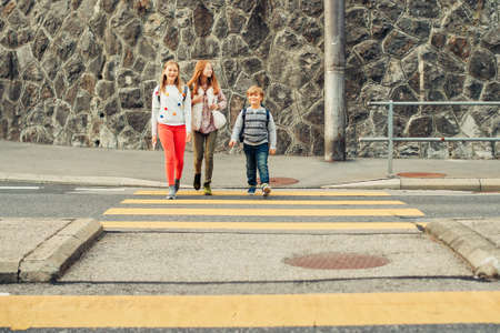 Group of 3 kids crossing the road, walking back to school, wearing backpacksの写真素材