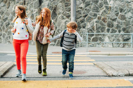 Group of 3 kids crossing the road, walking back to school, wearing backpacksの写真素材