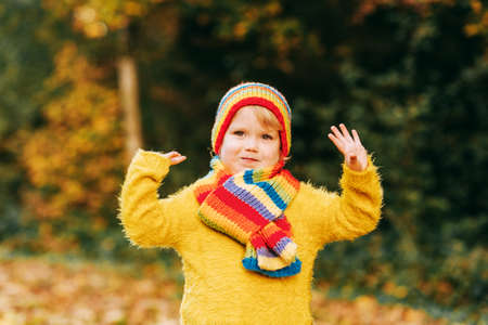 Outdoor portrait of cute toddler girl wearing yellow pullover, playing in autumn park
