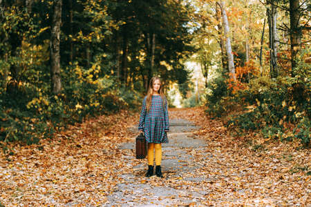 Autumn portrait of pretty young girl with old vintage suitcase, kid model posing outdoor in the...