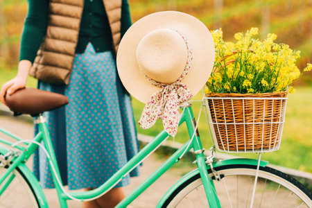 Woman holding vintage bicycle with hanging summer hat, yellow rapeseed flowers in wicker basketの写真素材