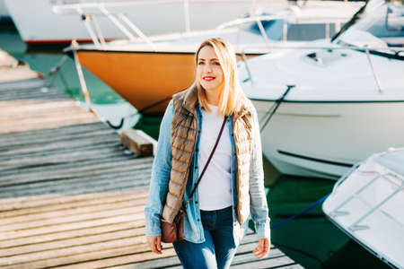 Outdoor fashion portrait of beautiful young woman posing by the lake in a small port