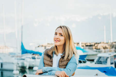 Outdoor fashion portrait of beautiful young woman posing by the lake in a small port