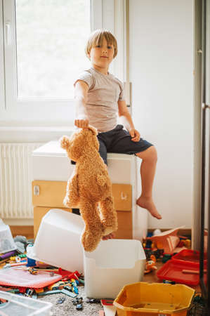 Indoor portrait of a child playing in a very messy room, throwing teddy bear on the floorの写真素材