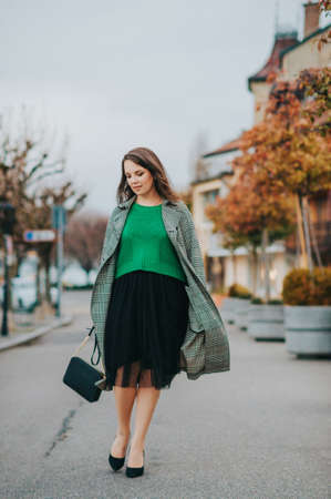 Outdoor portrait of beautiful woman wearing green pullover, black skirt and high heel shoesの写真素材
