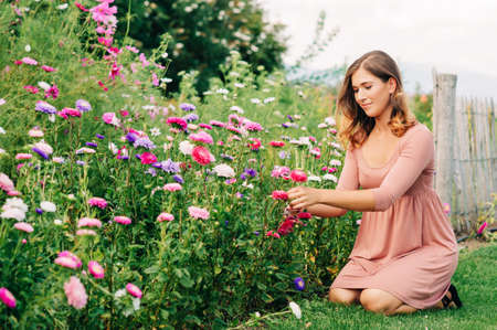 Pretty young woman working in autumn garden, girl taking care of colorful chrysanthemum, gardener enjoying warm and sunny dayの写真素材