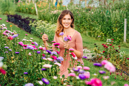 Pretty young woman working in autumn garden, girl taking care of colorful chrysanthemum, gardener...