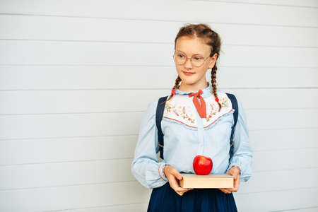 Happy little schoolgirl with book and red apple, wearing blue vintage blouse and  eyeglasses. Back to school conceptの写真素材