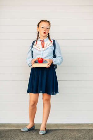 Happy little schoolgirl with book and red apple, wearing blue vintage blouse and  eyeglasses. Back...