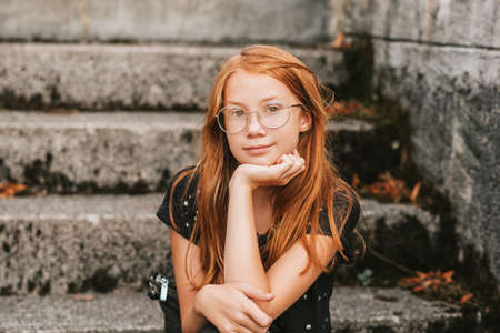 Outdoor portrait of sweet little girl with red hair, wearing eyeglassesの写真素材