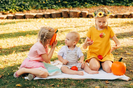 Autumn styled portrait for little kids, sisters and baby boy playing in sunny park with fall...