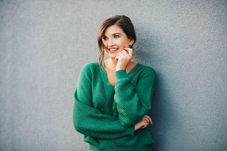 Outdoor portrait of beautiful young woman with wavy hairstyle, wearing knitted green pulloverの写真素材