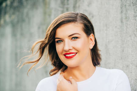 Outdoor portrait of beautiful young woman with wavy hairstyle, bright makeup red lipstick