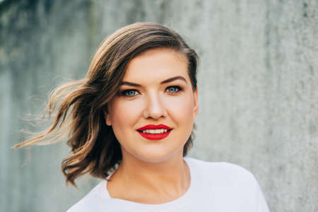 Outdoor portrait of beautiful young woman with wavy hairstyle, bright makeup red lipstick