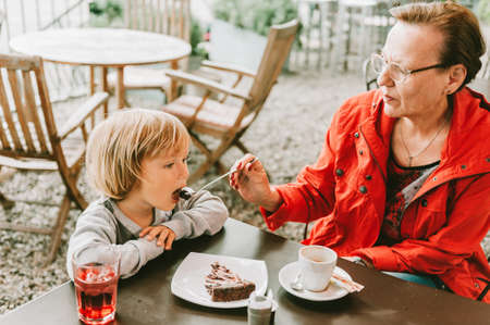Grandmother and little toddler boy spending time together in outdoor cafe, eating chocolate cake, family relationsの写真素材