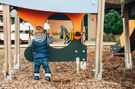 Cute toddler boy having fun on playground, cold weather day, back view