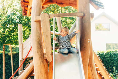 Outdoor portrait of happy toddler girl playing on playground, active child having fun in kids parkの写真素材