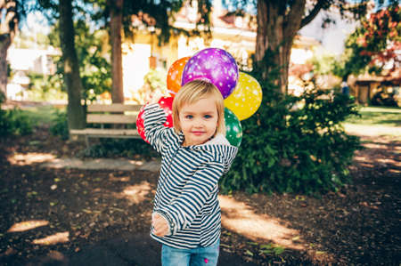 Funny kid girl playing with colorful balloons on playground