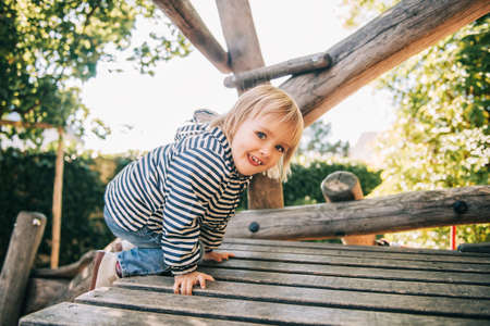 Outdoor portrait of happy toddler girl playing on playground, active child having fun in kids parkの写真素材