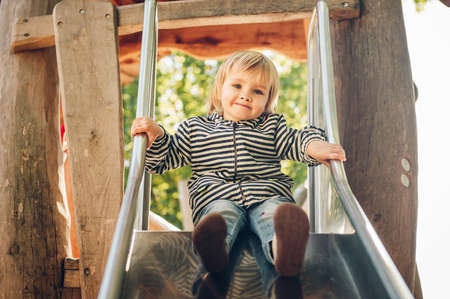 Outdoor portrait of happy toddler girl playing on playground, active child having fun in kids parkの写真素材
