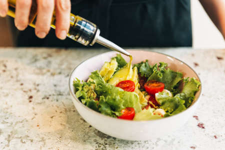 Fresh green salad with cherry tomatoes and avocado, waiter dressing salad with olive oilの写真素材