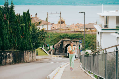 Portrait of young beautiful fit woman running up the hill, wearing green activewear, athlete model posing outdoors, sport fashionの写真素材