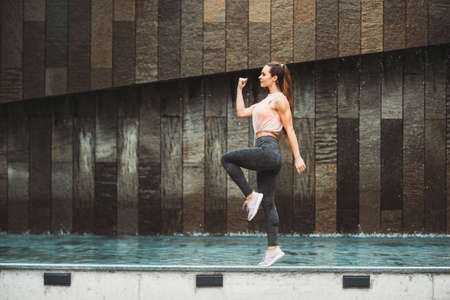Outdoor portrait of young beautiful fit woman stretching legs, wearing fashionable activewear,...
