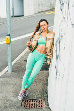 Outdoor portrait of young beautiful fit woman, wearing green activewear, athlete model posing next...