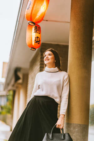 Outdoor street style portrait of young fashion woman, wearing warm turtle neck pullover and black skirt, hiding from rainの写真素材