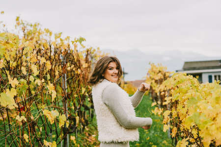 Autumn portrait of happy young woman enjoying nice day in vineyards, wearing grey pullover and fluffy white jacketの写真素材